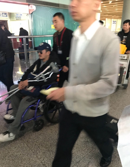 吴京手拿拐杖坐轮椅现身机场 表情严肃疑似腿受伤